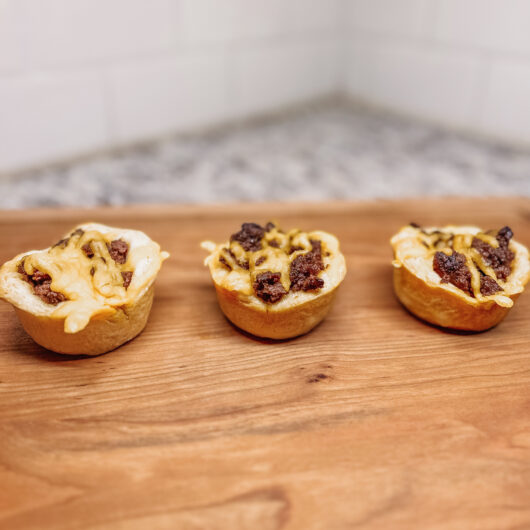three cheeseburger bites on a a wooden cutting board.