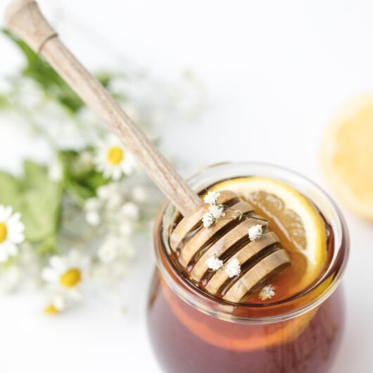 honey dipper on top of a jar of honey with little flowers on top.