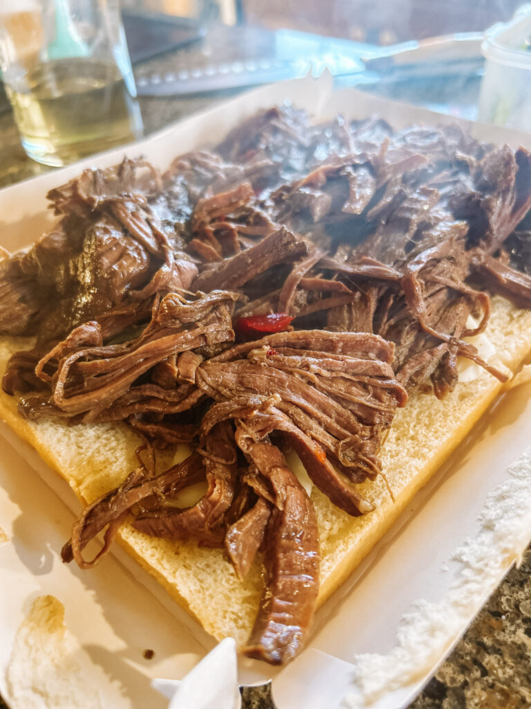 Shredded beef and peppers on a layer of bread on white cardboard