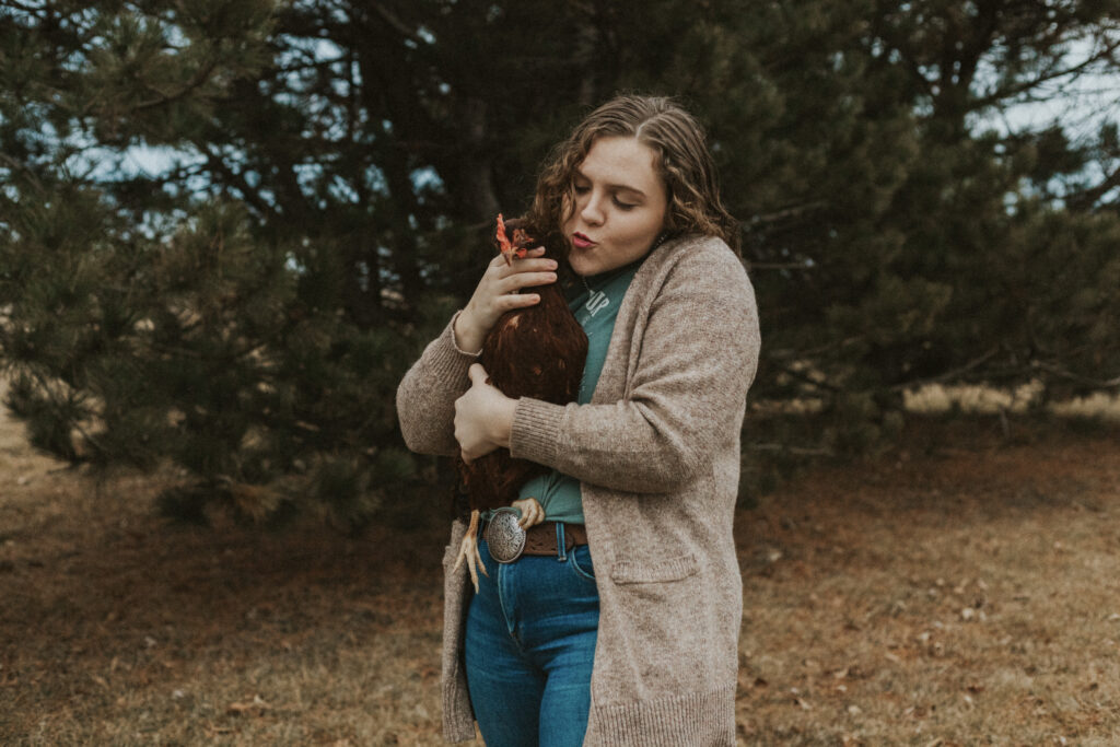 Female in a brown cardigan holding a chicken.