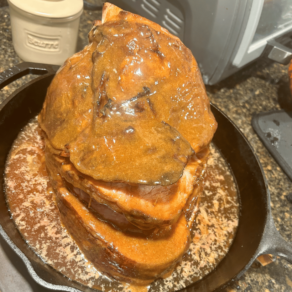 Ham in a cast iron skillet with glaze over it.